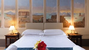 Una habitación de hotel con una cama grande, dos mesitas de noche con lámparas y un mural de un paisaje costero en la pared.