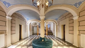 Un pasillo amplio con piso de cuadros, un pilar central y un candelabro.