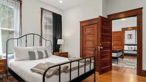 A bedroom with a metal bed frame, a wooden door, a nightstand, and a window with curtains. - The Bold City Retreat #327 - Team Joseph Ellen (Jacksonville)