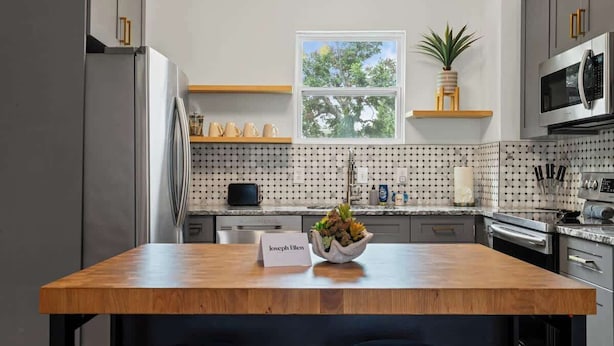 A modern kitchen with a wooden island, stainless steel appliances, and a window with a view of trees. - The Bold City Retreat #327 - Team Joseph Ellen (Jacksonville)