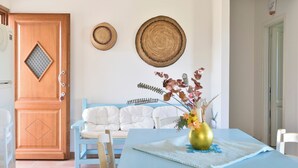 A room with a wooden door, a blue sofa, a table with a vase, and two woven wall hangings. - Villa Menhir! Exclusive property close to the beach (Lotzorai)