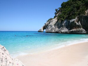 Une plage bordée d’une eau turquoise et limpide, d’une falaise rocheuse et d’un rivage sablonneux.