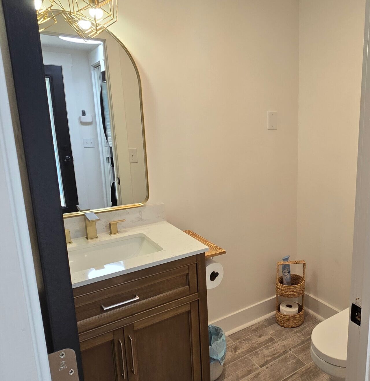A bathroom with a white sink, wooden vanity, a large mirror, and a toilet.