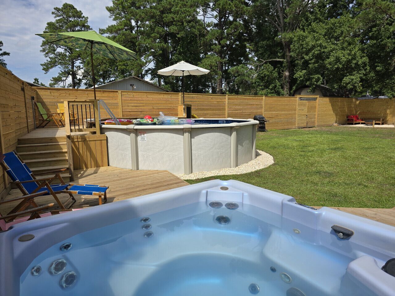 A backyard with a hot tub, wooden deck, and a covered seating area.