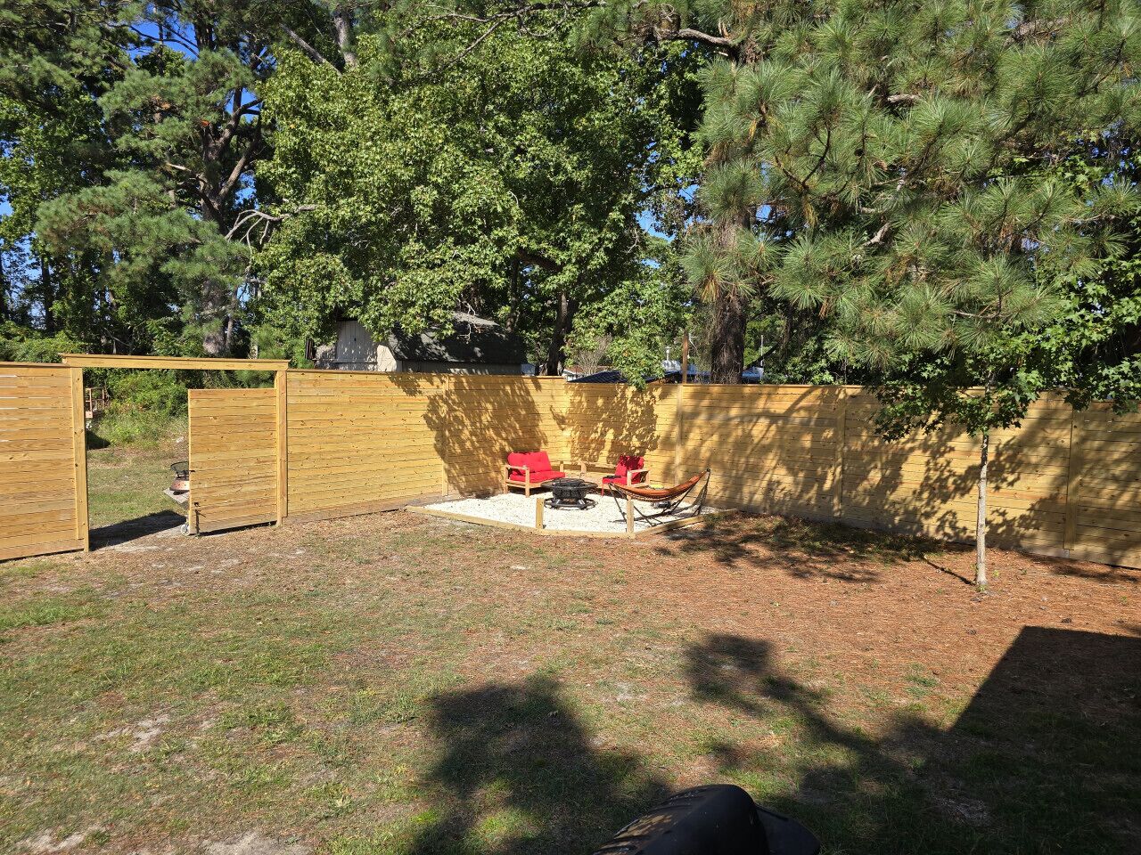 A backyard with a wooden fence, a red chair, a fire pit, and a small tree.