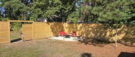 A backyard with a wooden fence, a red chair, a fire pit, and a small tree.