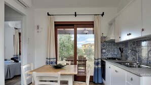 A kitchen with a dining area, a view to the outside, and a tiled backsplash. - Villa Menhir! (Lotzorai)