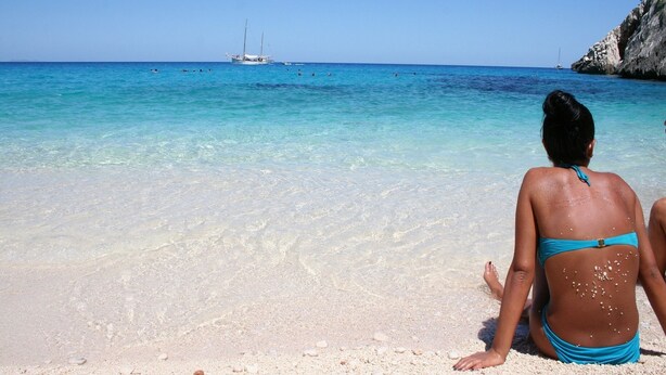 A beach with clear turquoise water, a rocky cliff, and a boat in the distance. - Villa Menhir! (Lotzorai)
