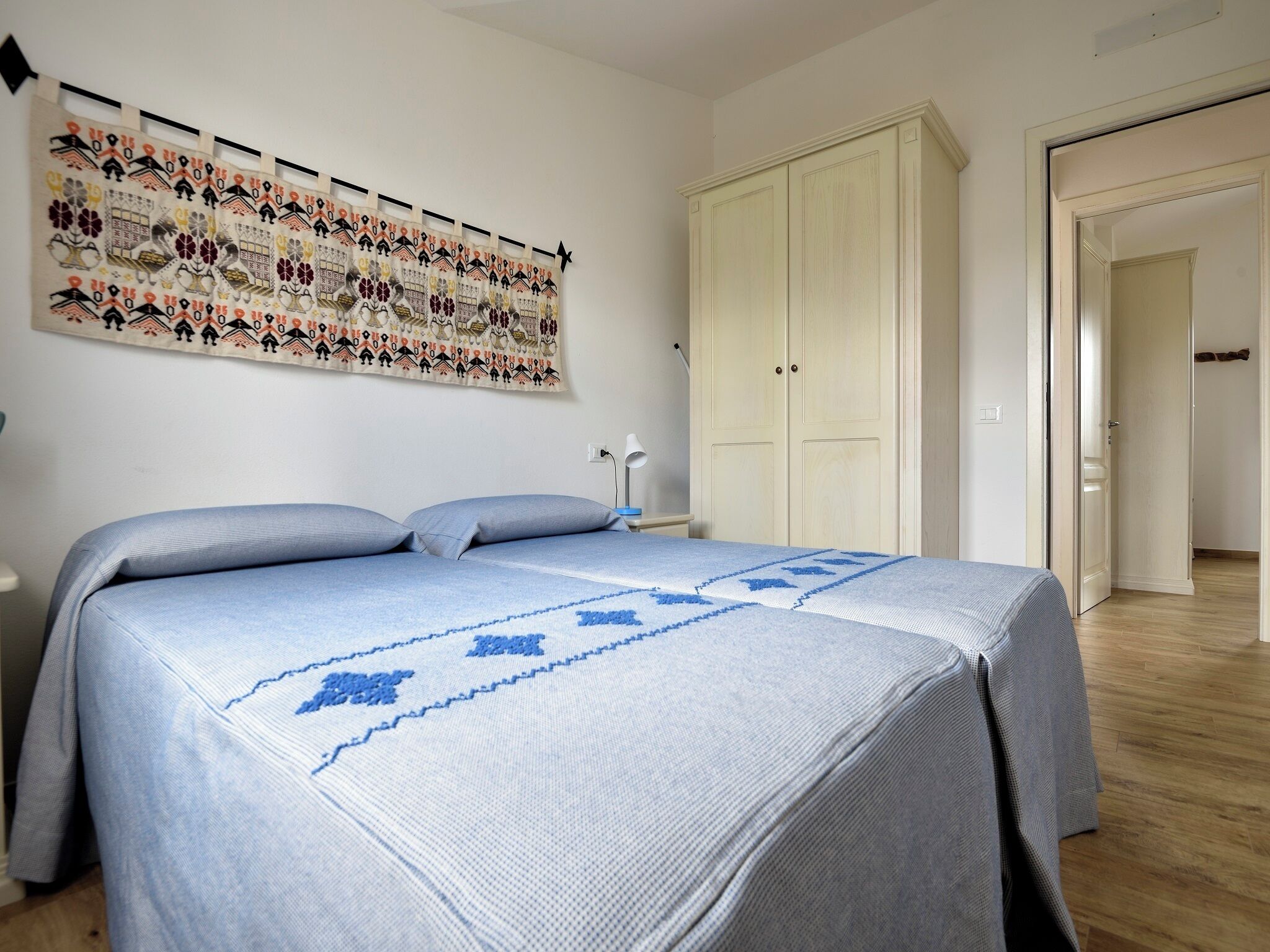 Ein Schlafzimmer mit Bett, Kleiderschrank, Wandteppich und einer Tür zu einem anderen Raum.