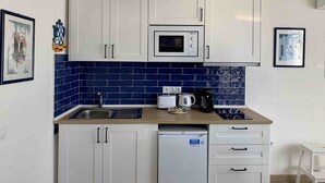 Una cocina compacta con gabinetes blancos, microondas, lavavajillas y salpicadero con azulejos azules.