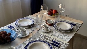 Una mesa de comedor dispuesta con platos, vasos y cubiertos, con un cuenco de uvas y una fuente de fruta sobre la mesa.