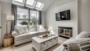 Una sala de estar moderna con un sofá, una mesa de centro, una chimenea y un televisor montado en la pared.