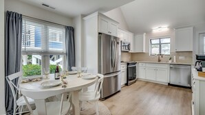 Una cocina moderna con armarios blancos, un refrigerador de acero inoxidable y un comedor con mesa dispuesta para cuatro.