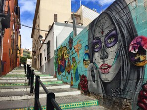 A street with a mural on the wall, steps leading up to a building, and a fence. - Charming Studio in Malaga City Center – Walk to Attractions, Restaurants, and Beach (Málaga)