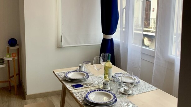 Ein Esstisch ist gedeckt mit Tellern, Gläsern und einer Flasche, nahe eines Fensters mit Vorhang.