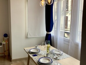 Ein Esstisch ist gedeckt mit Tellern, Gläsern und einer Flasche, nahe eines Fensters mit Vorhang.