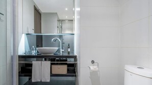 A modern bathroom with a glass-enclosed sink, a toilet, and a towel rack.