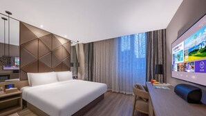 A modern hotel room with a large bed, a desk with a chair, a TV, and a large window with curtains.
