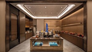 A modern hotel lobby with a central reception desk, a decorative blue sculpture, and a row of copper pots on the wall.