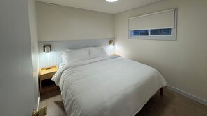A bedroom with a single bed, a nightstand, a wall-mounted light, and a window with blinds.
