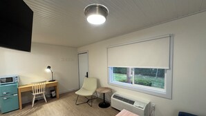 A modern room with a wooden desk, a chair, a small table, a heater, and a window with a view of greenery.