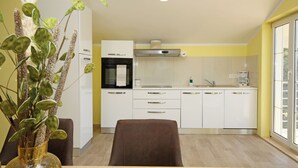 Una cocina moderna con armarios blancos, una campana extractora de acero inoxidable y un comedor con una silla marrón y un jarrón con plantas verdes.
