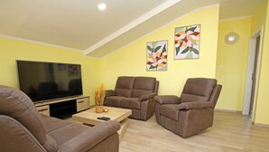 Una sala de estar con un televisor de pantalla plana, dos sofás marrones, una mesa de centro y dos cuadros con motivos florales en la pared.
