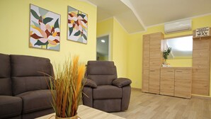 Un salón con dos sofás marrones, una mesa de centro con un control remoto y dos cuadros florales en la pared.