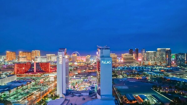 Uma paisagem urbana noturna com edifícios imponentes, incluindo uma construção alta com a sinalização 'PALMS'.