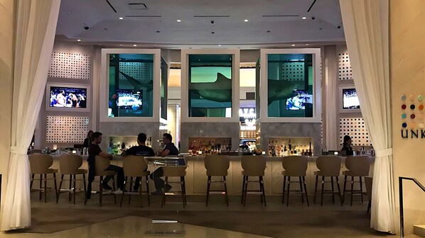 A bar area with multiple screens displaying content, bar stools, and a seating area with tables and chairs.