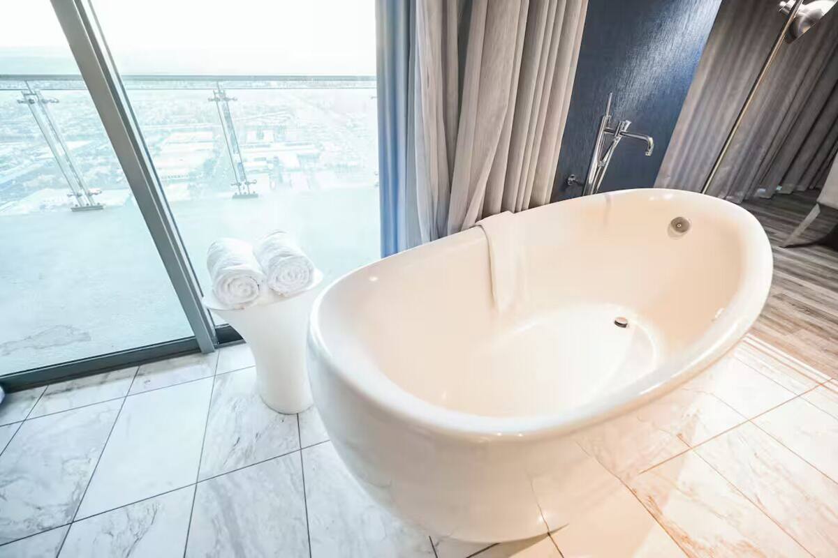 Une salle de bain moderne avec une baignoire sur pieds, une douche à parois de verre et une vue sur le paysage urbain grâce à de grandes fenêtres.