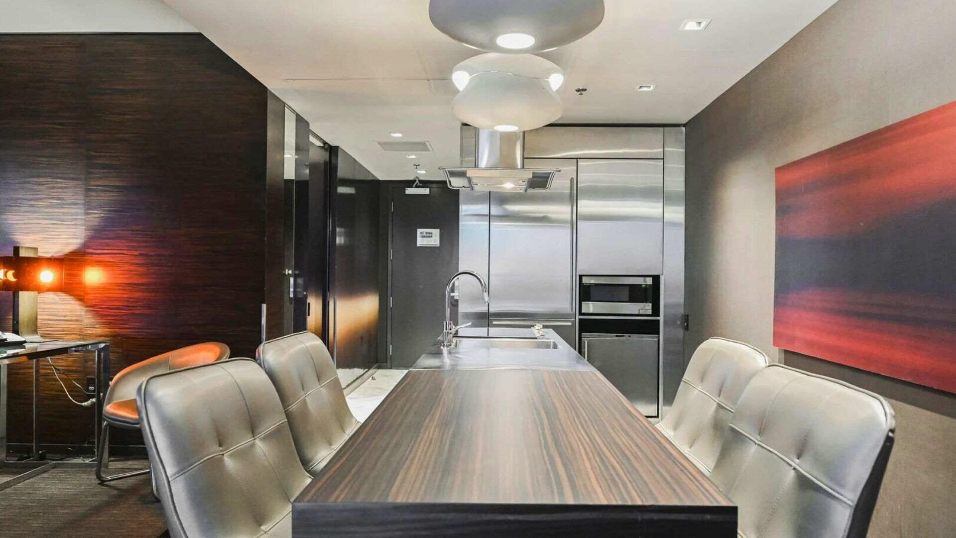 A modern conference room with a long table, leather chairs, a built-in sink, and a stainless steel refrigerator.