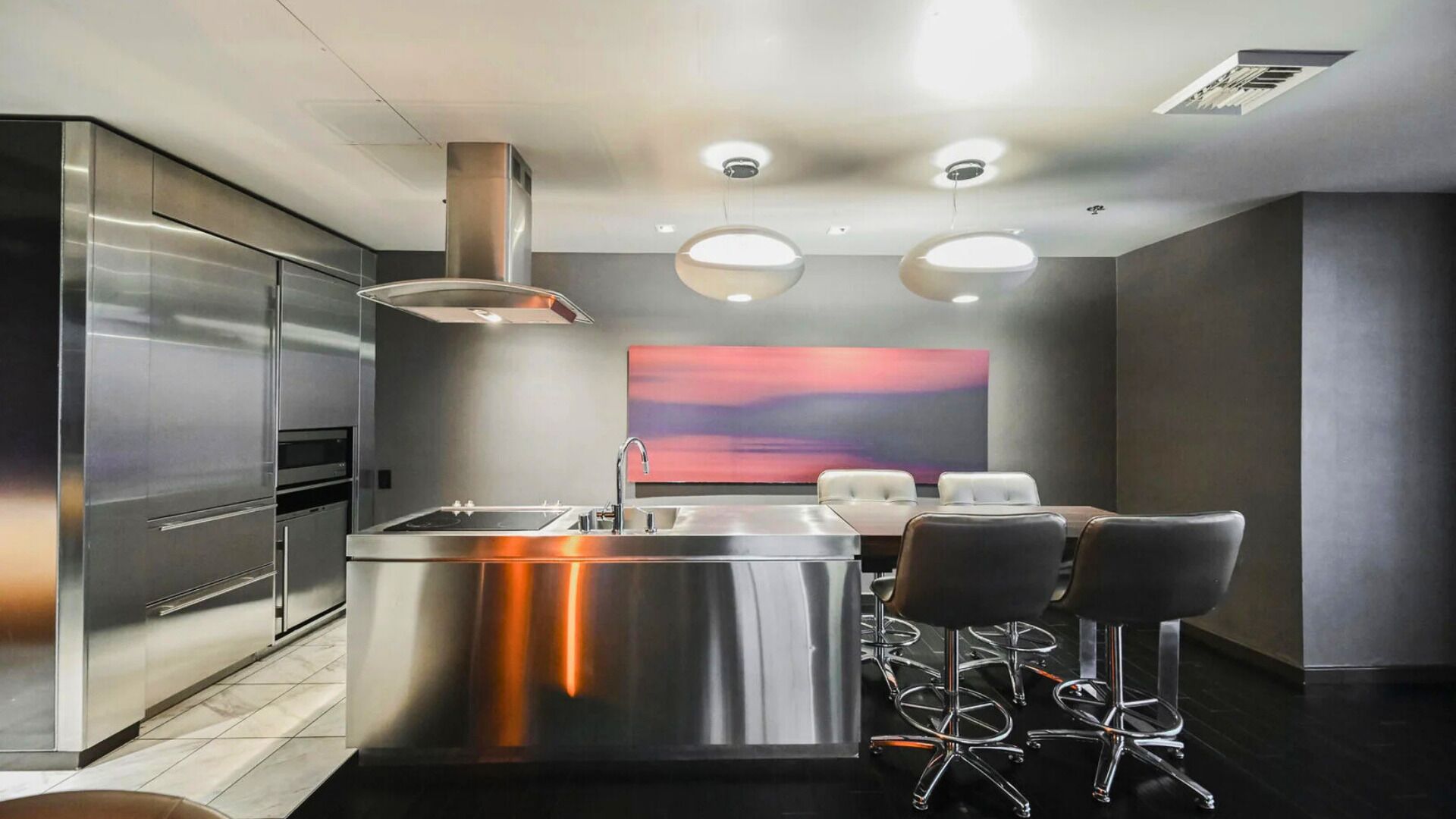 Une cuisine moderne dotée d’appareils électroménagers en acier inoxydable, d’un îlot central avec un évier et de tabourets de bar.