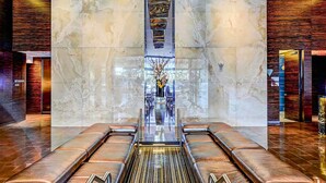 A modern lobby with a central elevator, glass walls, and a seating area with leather benches. - One Bedroom | 1.5 Baths & Living Room | Jet Tub – Palms Place StripSuite- NO RESORT FEE (Las Vegas)