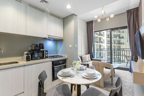 A modern kitchen with a dining area, including a round table set for four, a built-in oven, and a coffee maker.