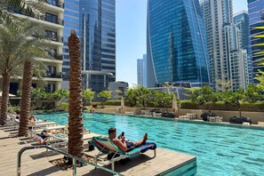 A poolside area with lounge chairs, palm trees, and modern high-rise buildings in the background.