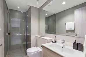 A modern bathroom with a glass-enclosed shower, a white toilet, a large sink, and a mirror above the sink.