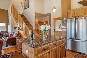 A kitchen with a granite countertop, wooden cabinets, a stainless steel refrigerator, and a wooden staircase.