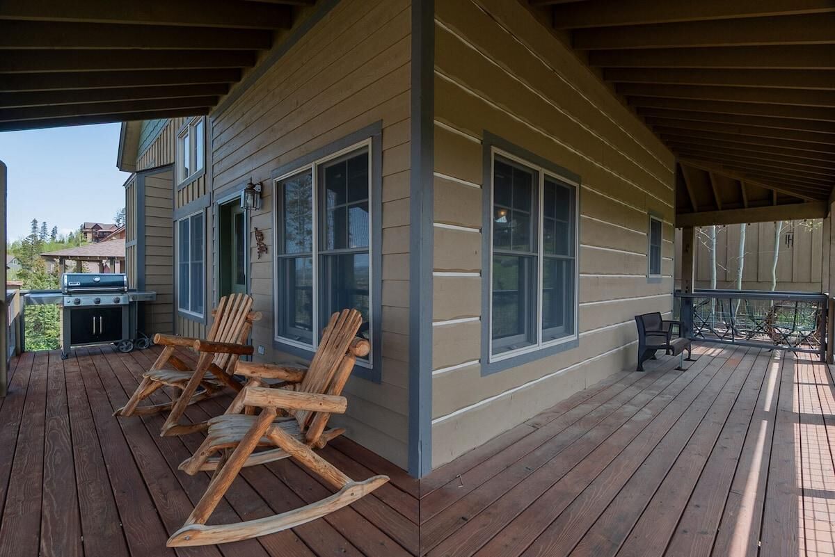 A covered porch with wooden rocking chairs, a grill, and a bench.
