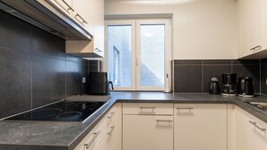 Una cocina moderna con encimera negra, armarios blancos, estufa integrada y una ventana con vistas a un edificio de ladrillo.
