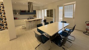 Una cuina moderna amb una illa central, tamborets d'abarco i una taula de dinar amb cadires.