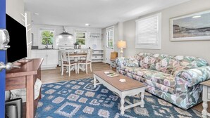 Ein modernes Wohnzimmer mit einer floralen Couch, einem Holztisch und einem Essbereich mit weißem Tisch und Stühlen.