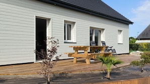 Una casa blanca con terraza de madera, una mesa de picnic y un pequeño jardín.