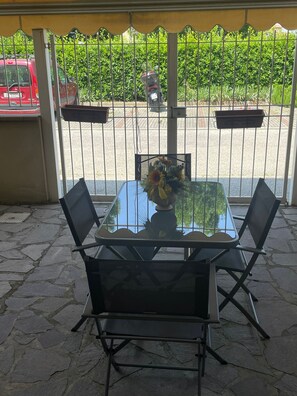 An outdoor patio with a glass table and four chairs, a flower vase, and a metal fence with greenery behind it. - A bright, cozy, and fully equipped apartment. (Firenze)
