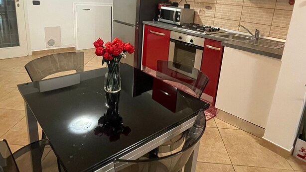 Une cuisine moderne avec des meubles de rangement rouges, une table à manger noire et un vase rempli de roses rouges.