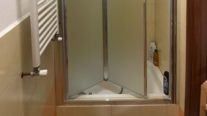 Une cabine de douche fermée par des parois en verre, avec un radiateur blanc sur la gauche et une bouteille de shampoing sur la droite.