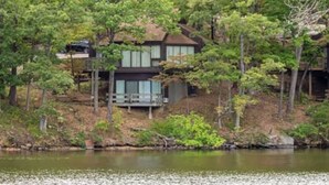 A lakeside cabin with a two-story structure, surrounded by dense forest.