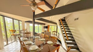 A dining area with a large wooden table set for six, surrounded by chairs. A staircase is visible to the right, leading to an upper level.