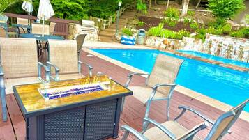 Un espace aménagé au bord de la piscine, avec une table et des chaises en bois, un jacuzzi et une piscine.