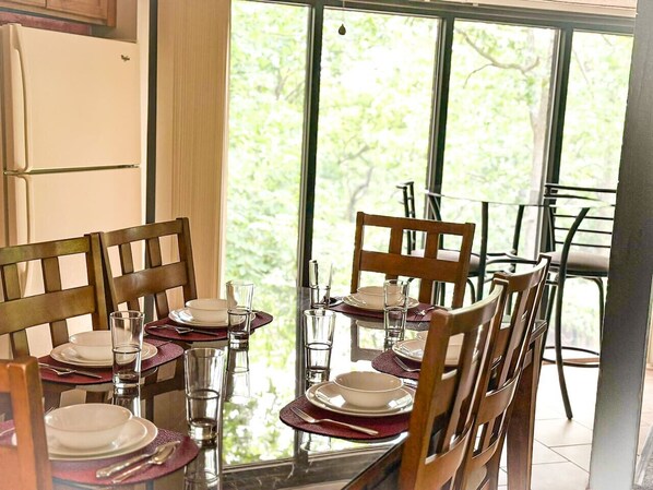 A dining area with a glass table set for four, surrounded by wooden chairs.